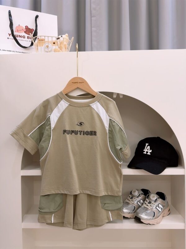 Grey-green T-shirt and shorts on a hanger, with white and green panels and FUFUTIGER lettering on the top and green patch pockets on the shorts; a black cap and trainers sit nearby.