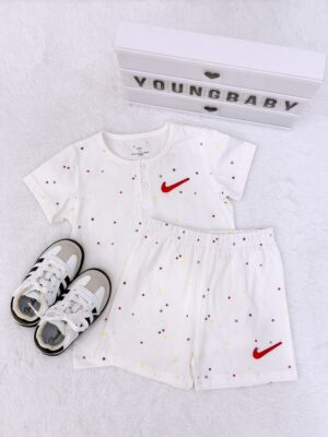 White short-sleeved top and elastic-waist shorts with multicoloured little stars and red check-shaped motifs, displayed beside trainers.