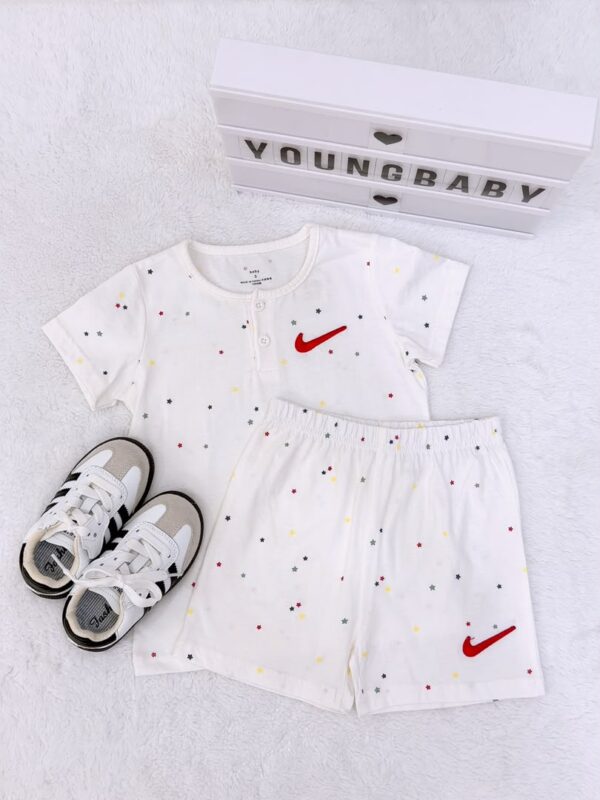 White short-sleeved top and elastic-waist shorts with multicoloured little stars and red check-shaped motifs, displayed beside trainers.