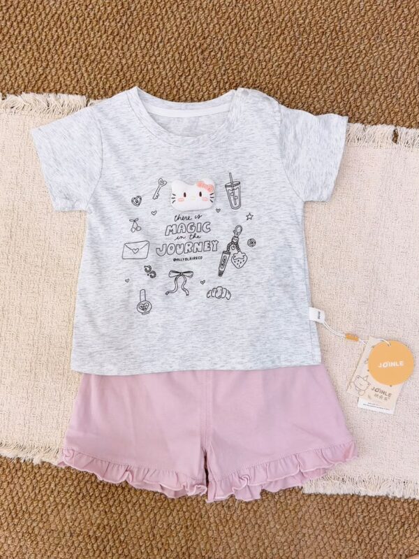 Light heather-grey short-sleeve top with a cartoon cat and small motifs, paired with pink ruffle-hem shorts.