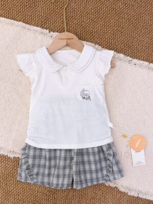 White rounded-collar top with flutter sleeves, two front buttons and a cartoon patch pocket, paired with black, white and grey checked shorts with side ruffles.