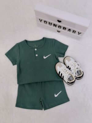 Dark green round-neck, two-button short-sleeve top and shorts with vertical texture and white tick-shaped motifs, with lace-up trainers on the right.