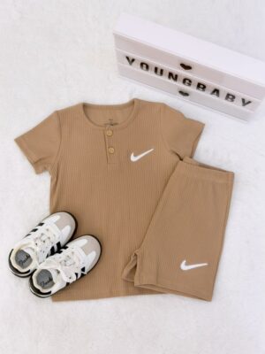 Camel brown round-neck, two-button short-sleeve top and folded shorts with vertical texture and white tick-shaped motifs, beside lace-up trainers.