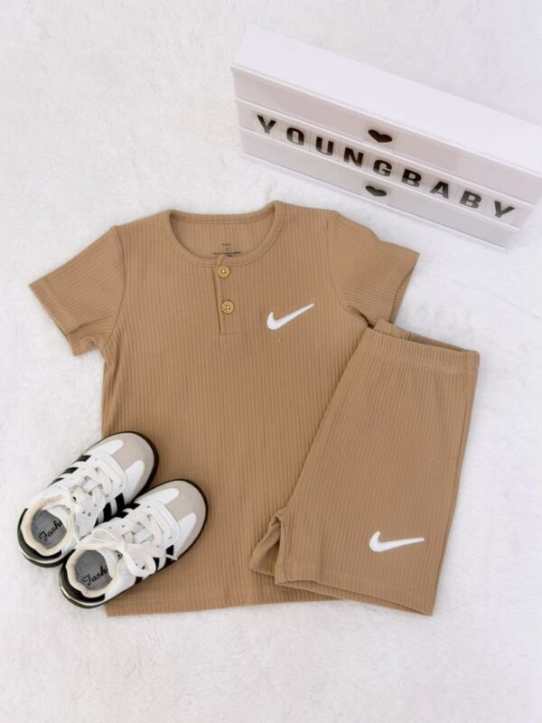 Camel brown round-neck, two-button short-sleeve top and folded shorts with vertical texture and white tick-shaped motifs, beside lace-up trainers.