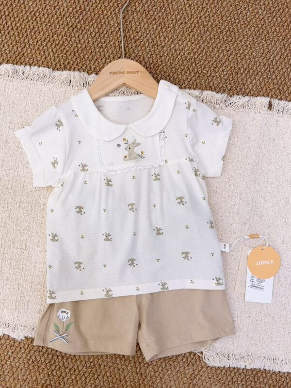 White rabbit-and-flower print short-sleeved top with a rounded collar and lace-edged rabbit chest panel, paired with beige-brown shorts featuring a white flower and green leaves.