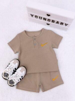 Taupe round-neck, two-button short-sleeve top and shorts with a fine grid-like texture and yellow tick-shaped motifs, beside lace-up trainers.