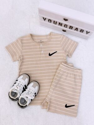 Beige round-neck, two-button short-sleeve top and folded shorts with white horizontal stripes and black tick-shaped motifs, beside lace-up trainers.