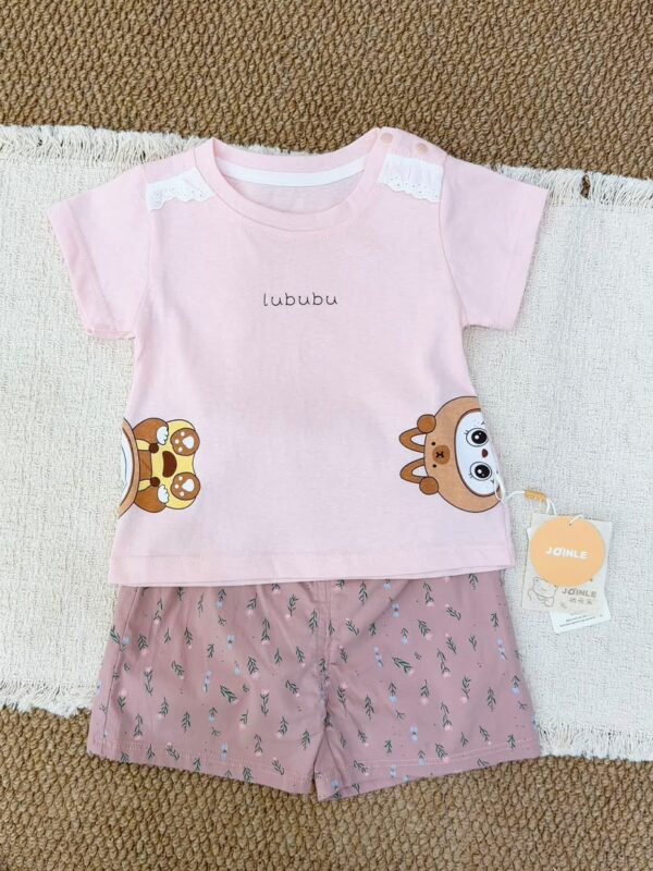 Pale pink crew-neck short-sleeved top with white shoulder lace, snap buttons and cartoon graphics at the lower sides, paired with dusty pink floral shorts.