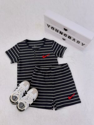 Near-black top and elastic-waist shorts with thin white stripes and red tick-shaped motifs, laid flat beside trainers and a YOUNGBABY lightbox. The short-sleeve top has a round neck and button placket.