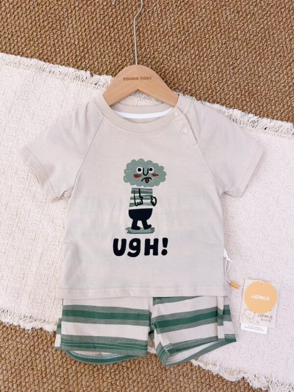 Light greige raglan short-sleeved top with shoulder snaps, a green cartoon character and large black lettering, paired with green and light greige striped shorts.